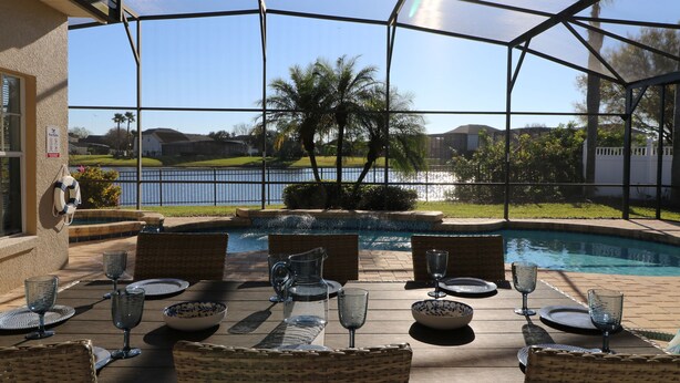 Uma área externa coberta com piscina, mesa de jantar posta com copos e cadeiras de vime.