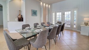 Uma área de jantar com mesa de vidro, cadeiras estofadas cinzas e uma porta branca que dá para o exterior.