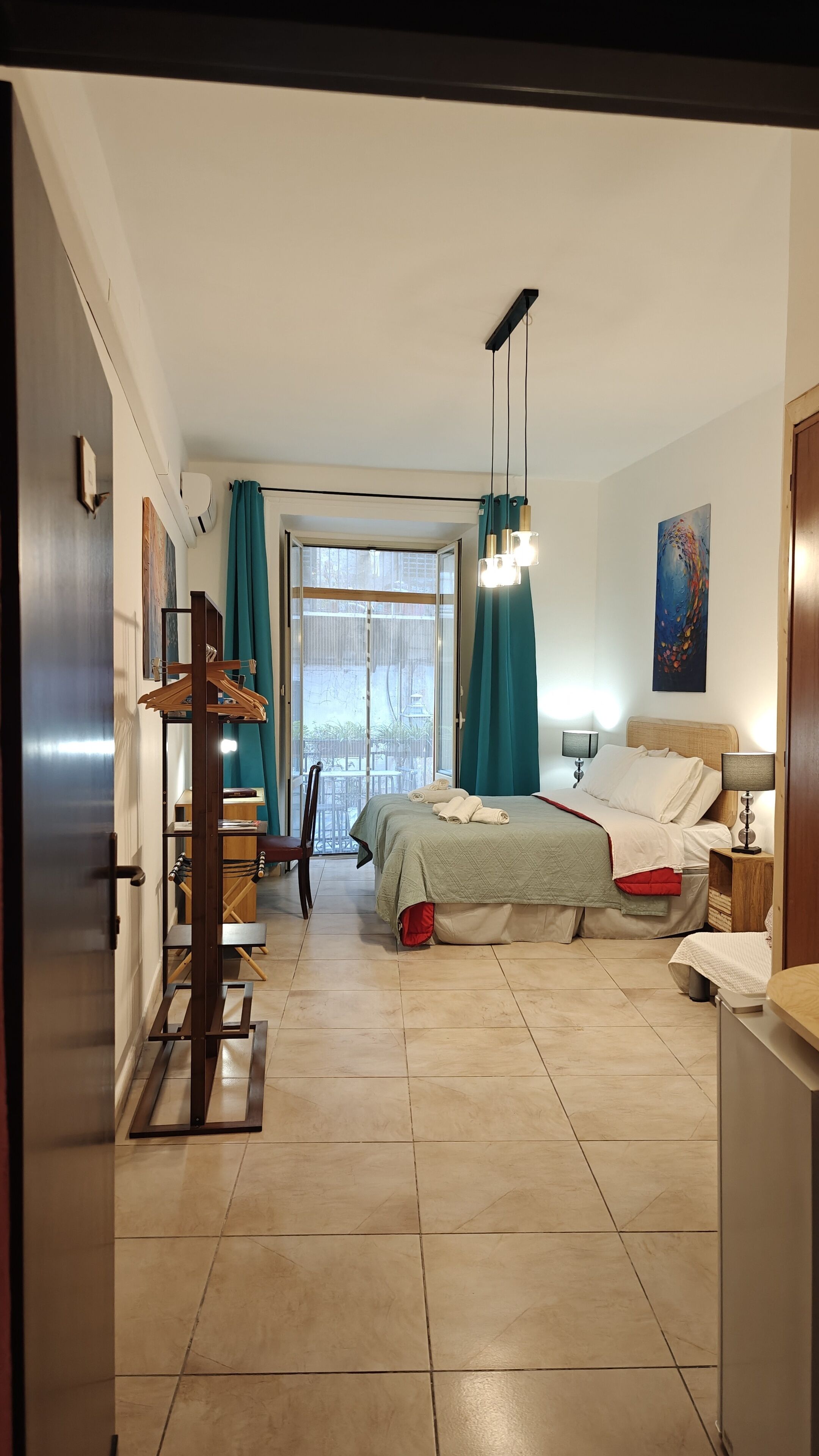 A hotel room with a bed, bedside tables, a desk, and a view of the outside.