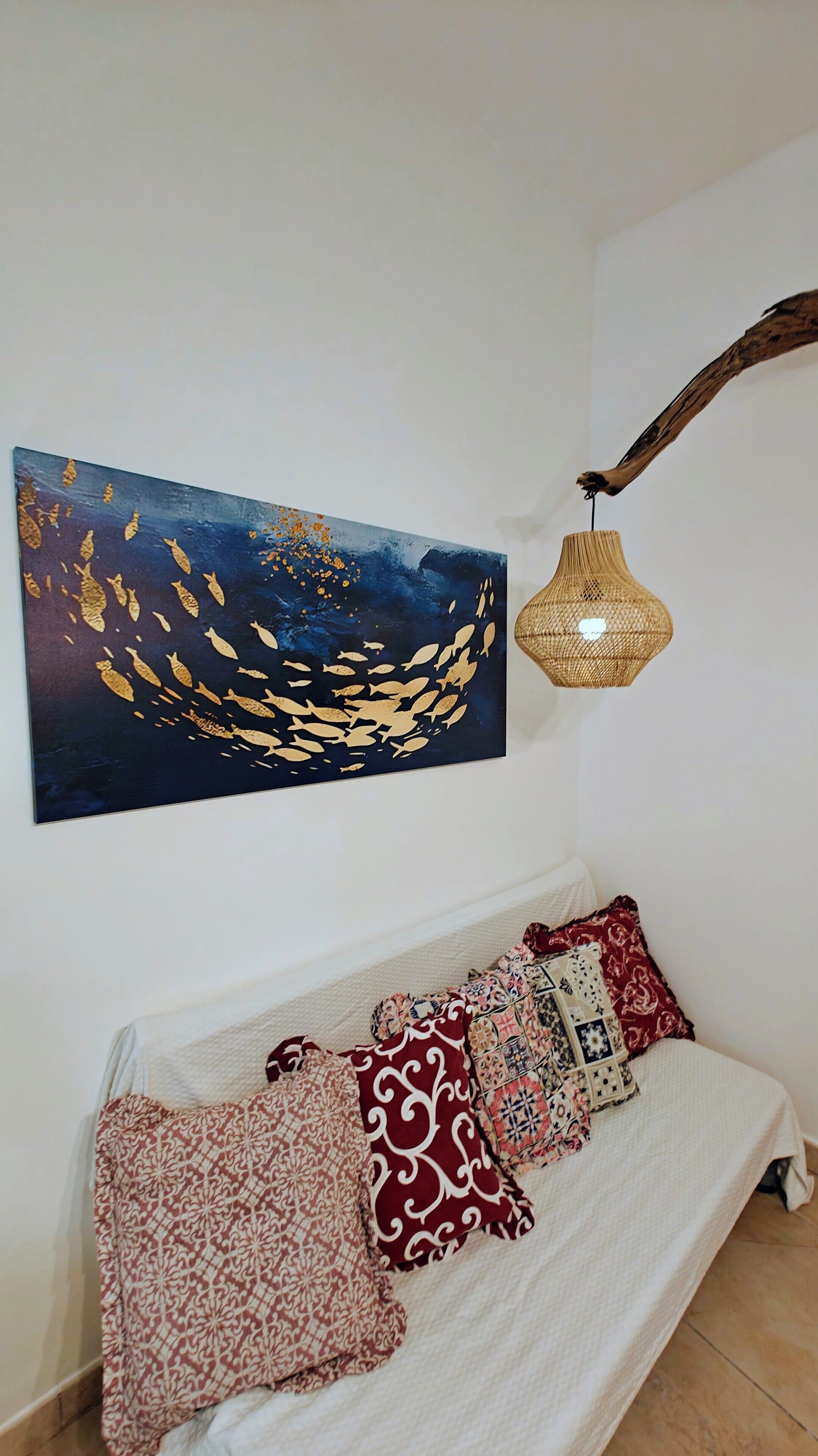 A room with a bed, a wall-mounted painting, and a hanging lamp.