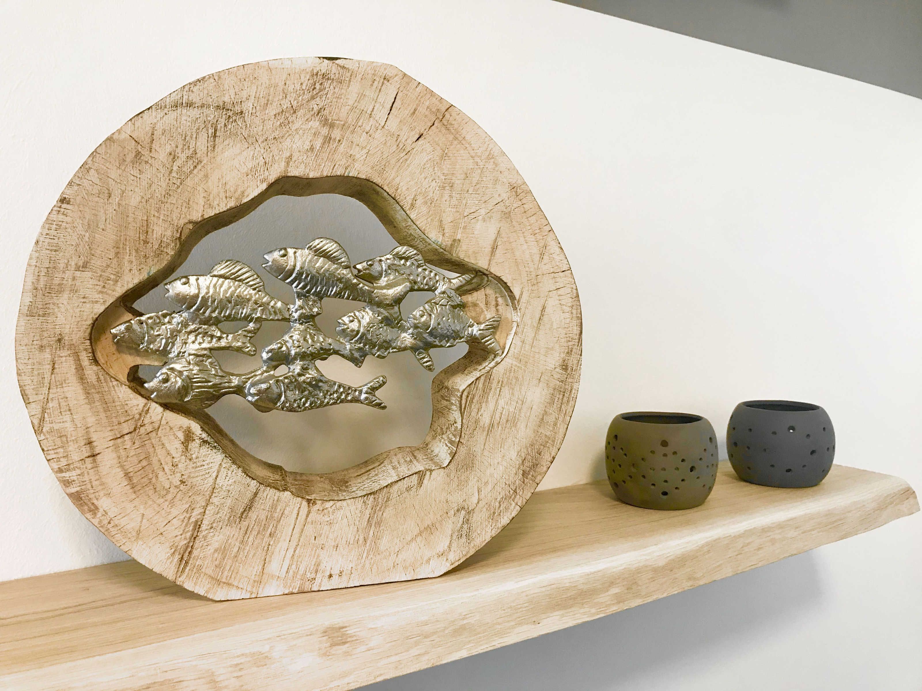 Een houten decoratief object met visgravures op een plank, samen met twee keramische bekers.