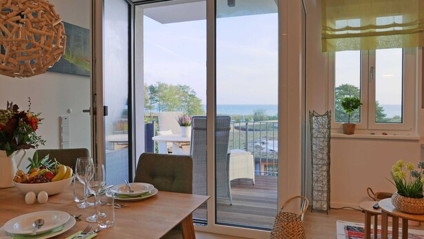 A dining area with a table set for two, a bowl of fruit, and a view of the sea through a sliding glass door. - Baabe Villen Ensemble FeWo 34 Pura Vida Ref. 215429 (Baabe)