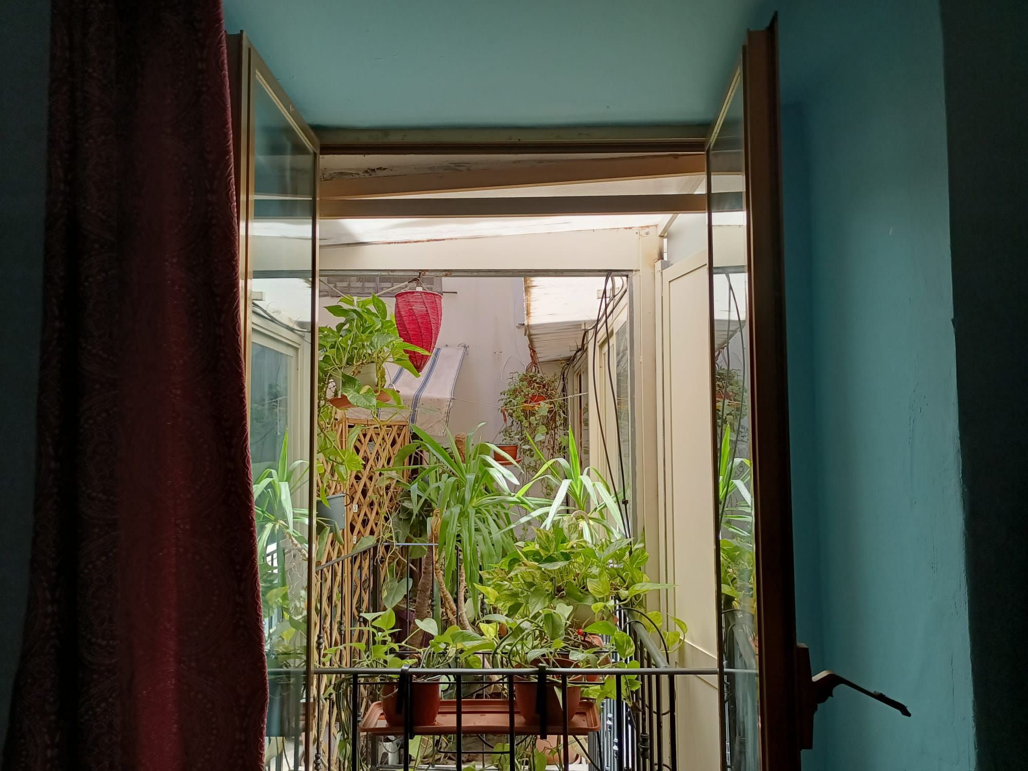 A balcony with potted plants, a red hanging lantern, and a view of a building in the background.