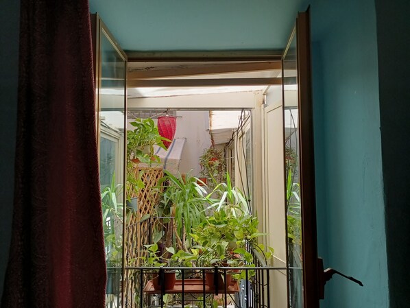 A balcony with potted plants, a red hanging lantern, and a view of a building in the background.