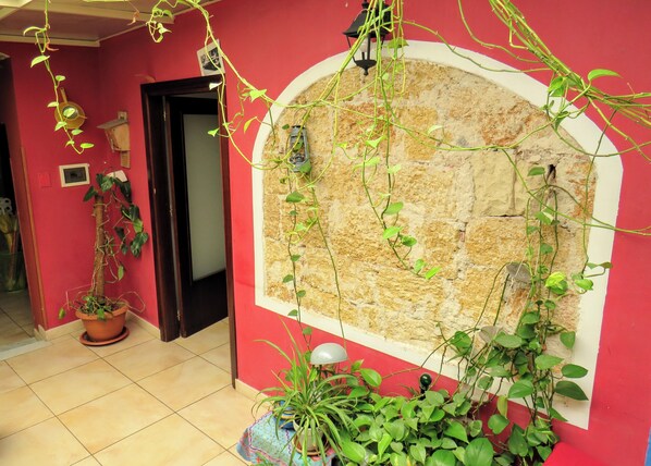 A room with a red wall, a stone archway, and various potted plants.
