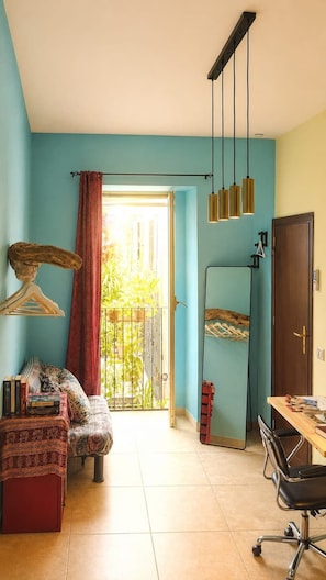A room with a sofa, a dining table, a mirror, and a hanging light fixture.