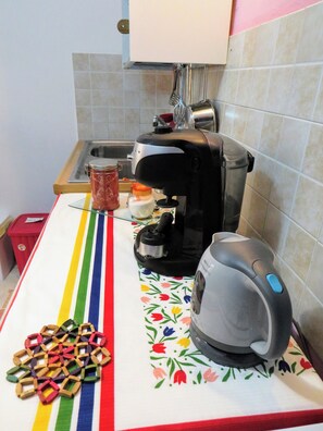 A kitchen with a coffee maker, a jar of jam, and a colorful tablecloth.