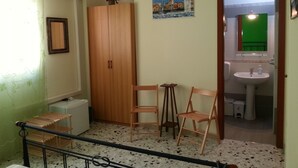 Una habitación con armario, dos sillas, una mesita y baño con lavabo y espejo.
