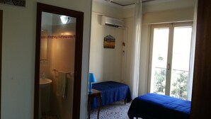 Un dormitorio con cama, una mesita, una silla, baño y balcón con vistas.