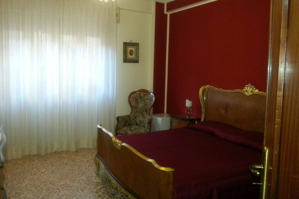 A bedroom with a wooden bed, a chair, a small table, and a picture on the wall.