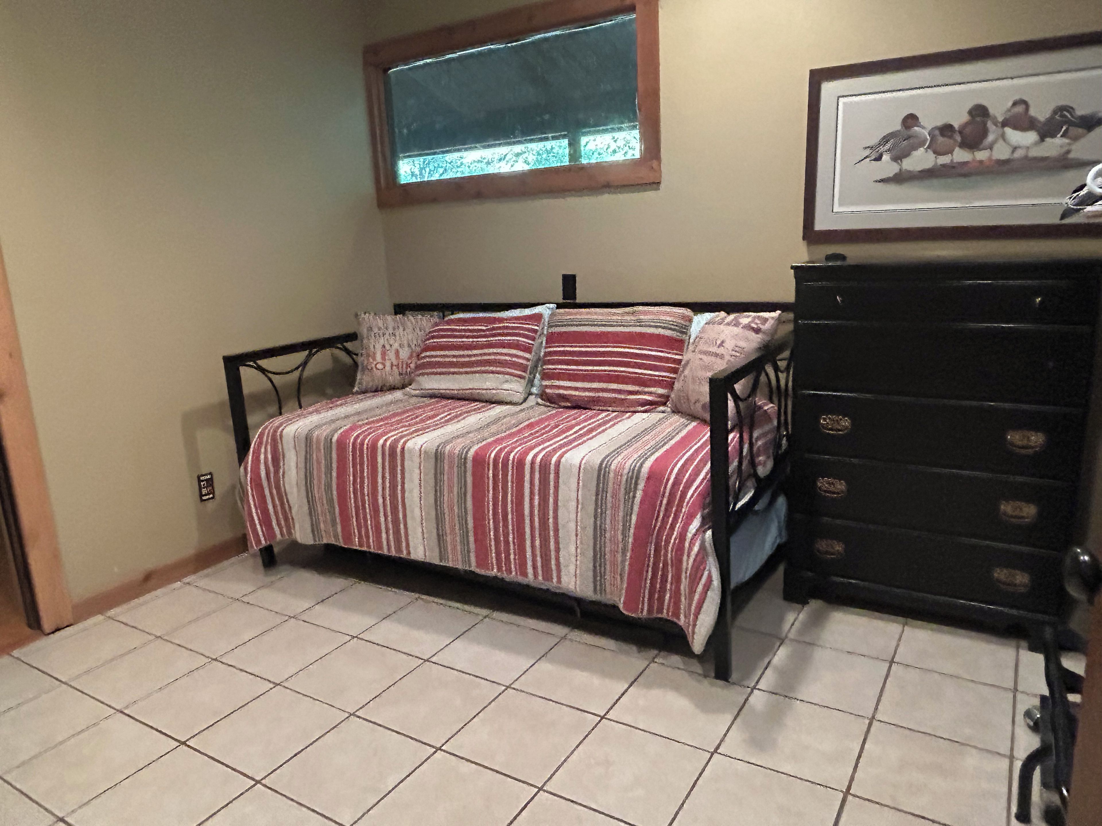 A bedroom with a bed, a dresser, a window, and a framed picture on the wall.