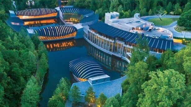 Vue aérienne d’un hôtel moderne composé de plusieurs bâtiments reliés entre eux, avec une cour centrale et une forêt luxuriante qui l’entoure.