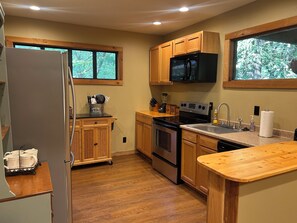 Una cocina con armarios de madera, un refrigerador de acero inoxidable, un microondas, un horno y un lavabo con encimera.