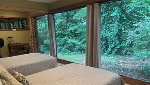 Une chambre avec deux lits, un bureau en bois, une chaise et une grande fenêtre avec des rideaux.
