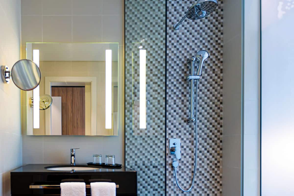 Une salle de bain moderne avec un grand miroir, un lavabo, deux serviettes, une douche et un mur à carreaux.