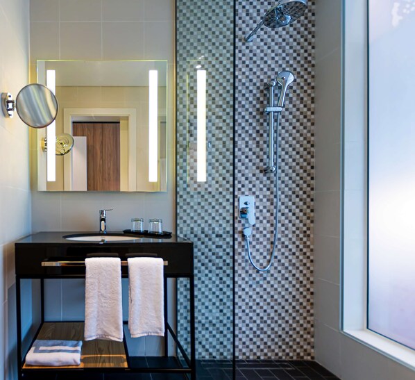 Un baño moderno con un espejo grande, un lavabo, dos toallas, una ducha y un pared con diseño a cuadros.