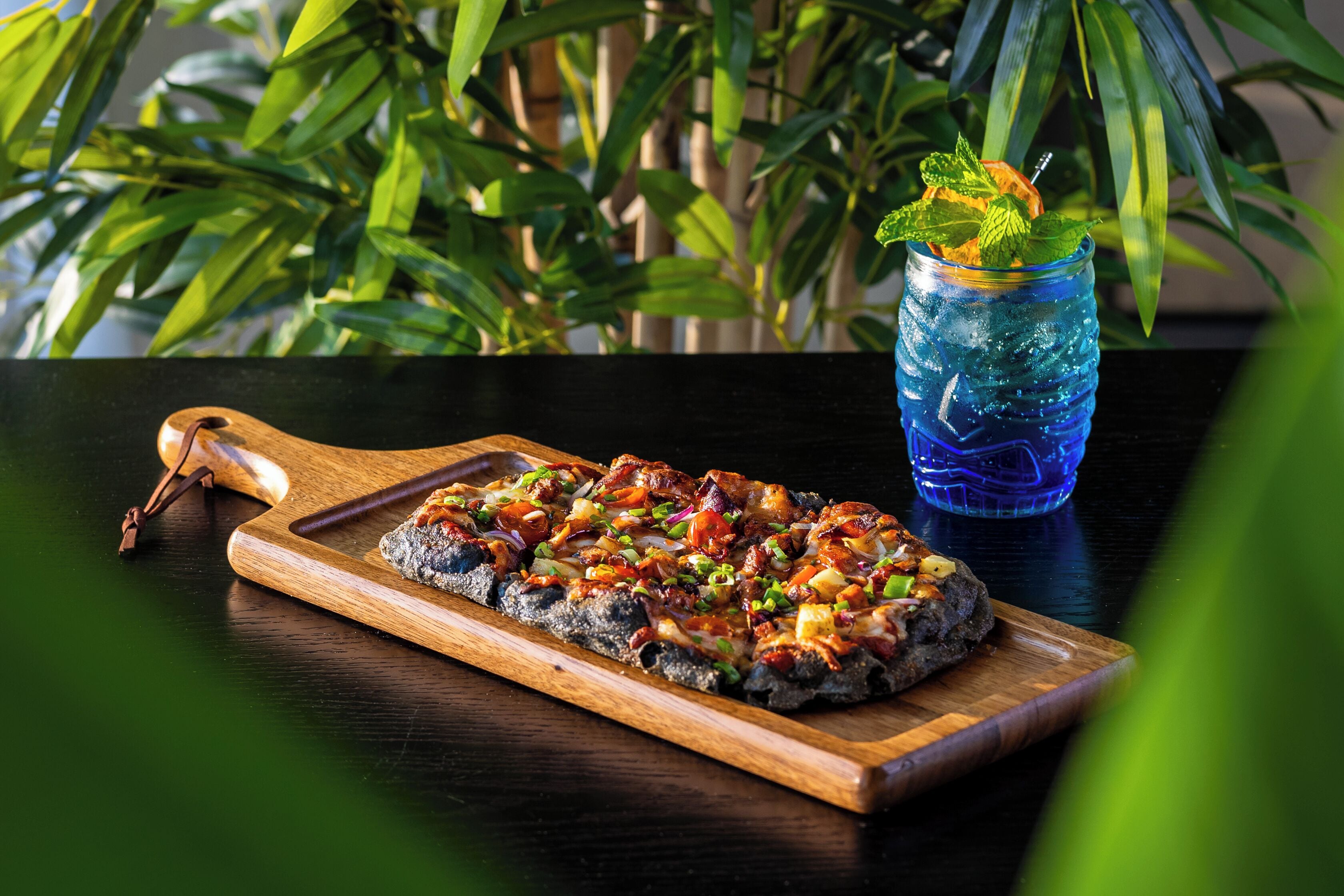 Una pizza sobre una tabla de madera con una bebida en un vaso.