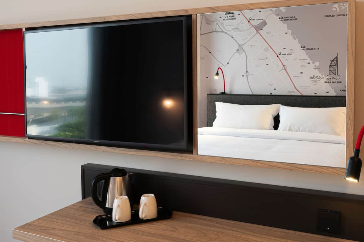 Une chambre d’hôtel dotée d’un grand téléviseur à écran plat, d’un lit avec une literie blanche, d’une carte accrochée au mur et d’un coin café.