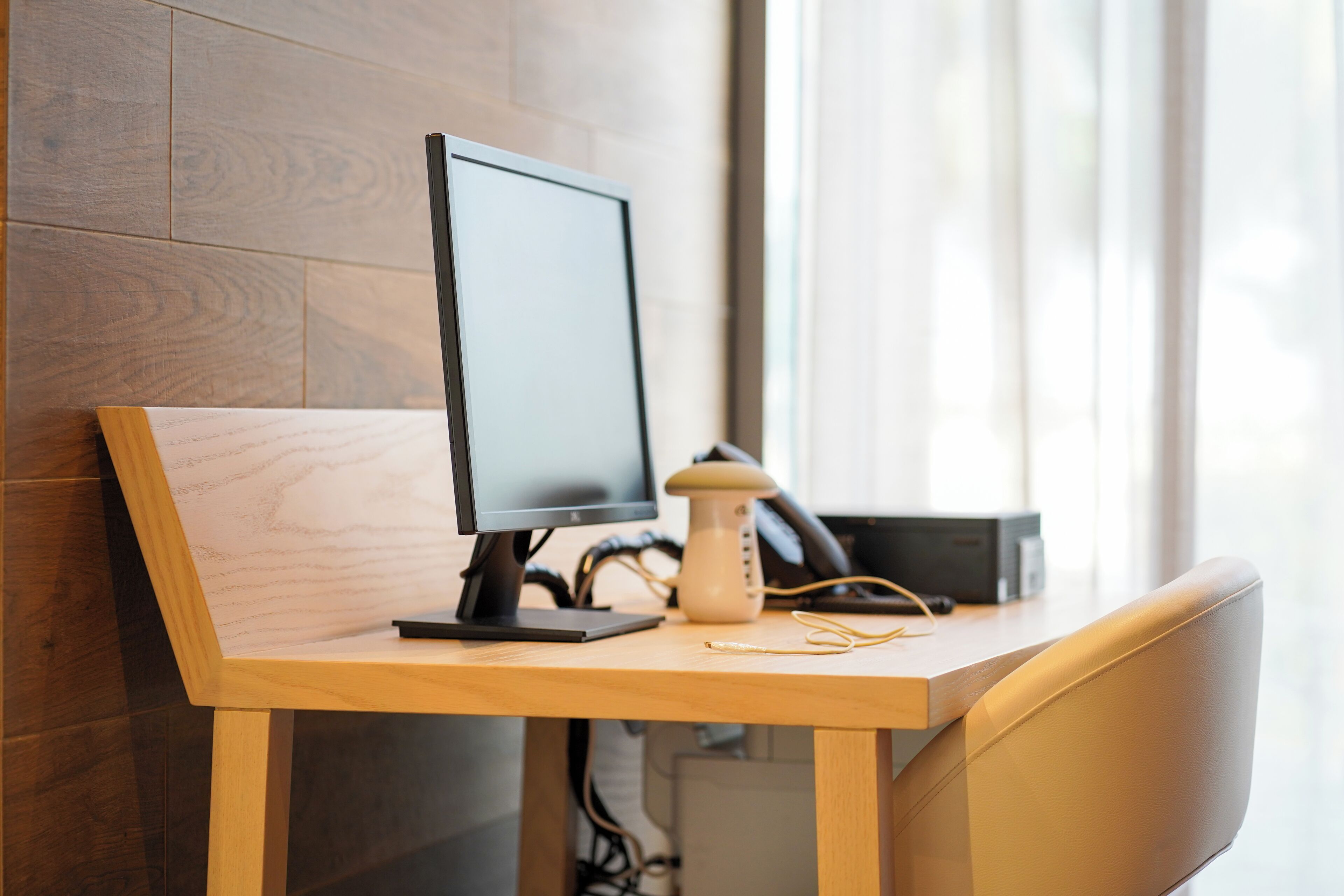 A wooden desk with a computer monitor, a lamp, and a pair of glasses.