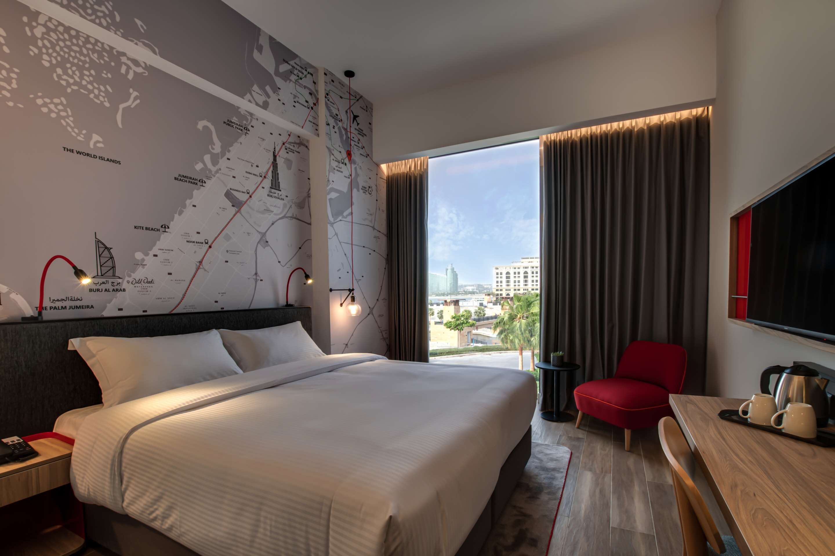 Habitación de hotel con una cama grande, un escritorio con una silla, un mapa en la pared y vistas a la ciudad.