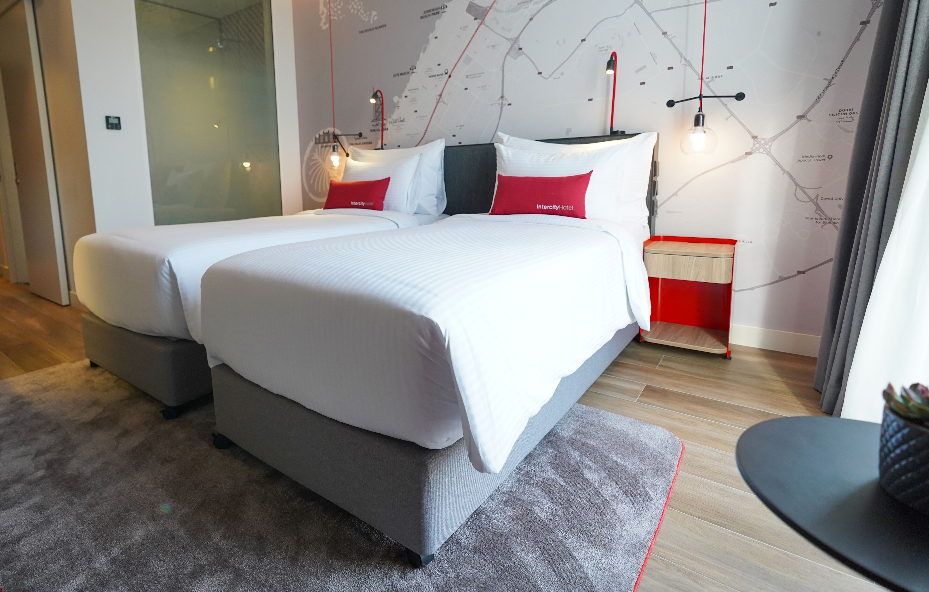 Ein modernes Hotelzimmer mit zwei Betten, einer Wand mit einer Weltkarte und einem kleinen Tisch mit einer Pflanze.