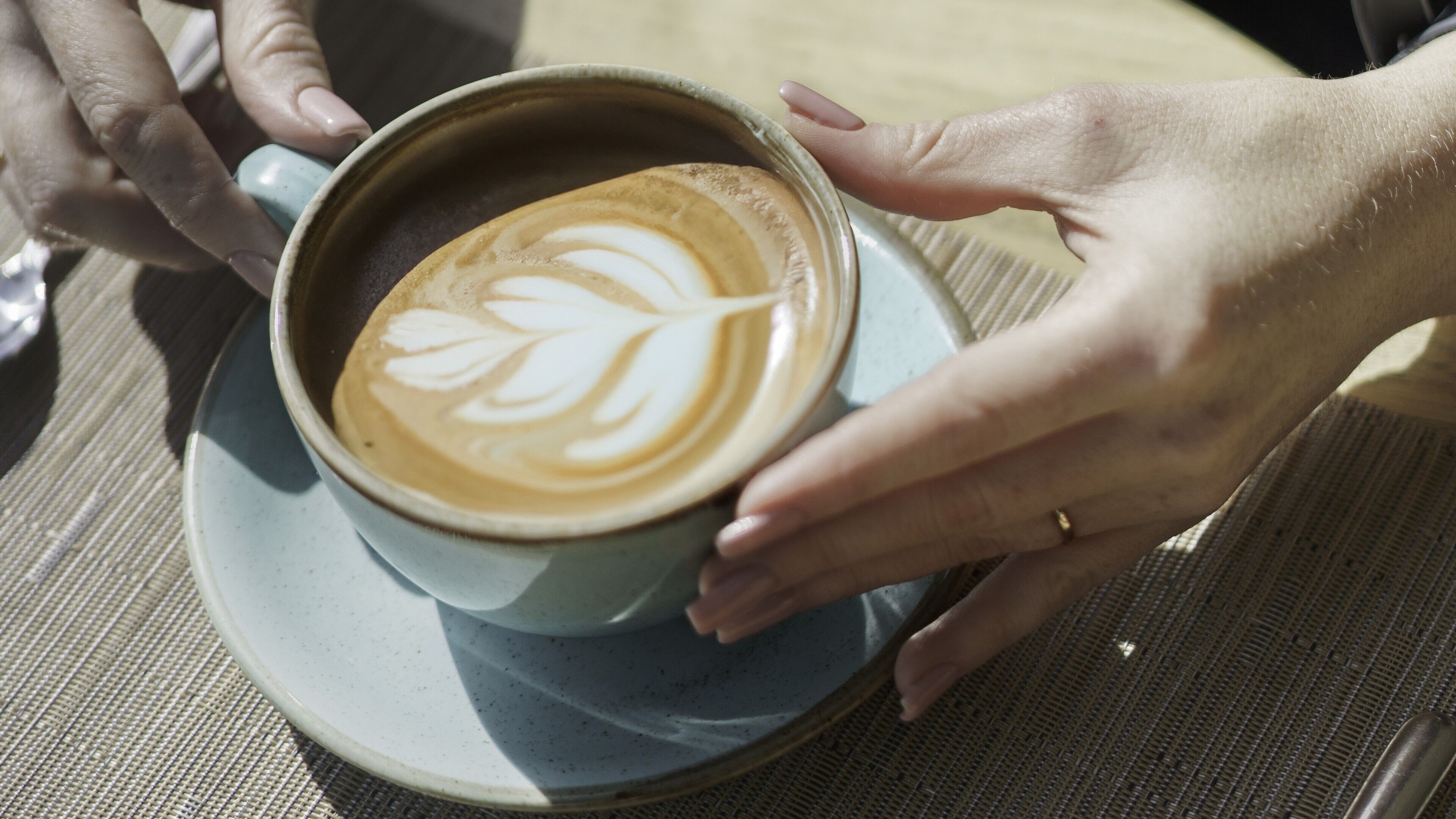 Koffie met een bladmotief in het schuim, vastgehouden door handen.