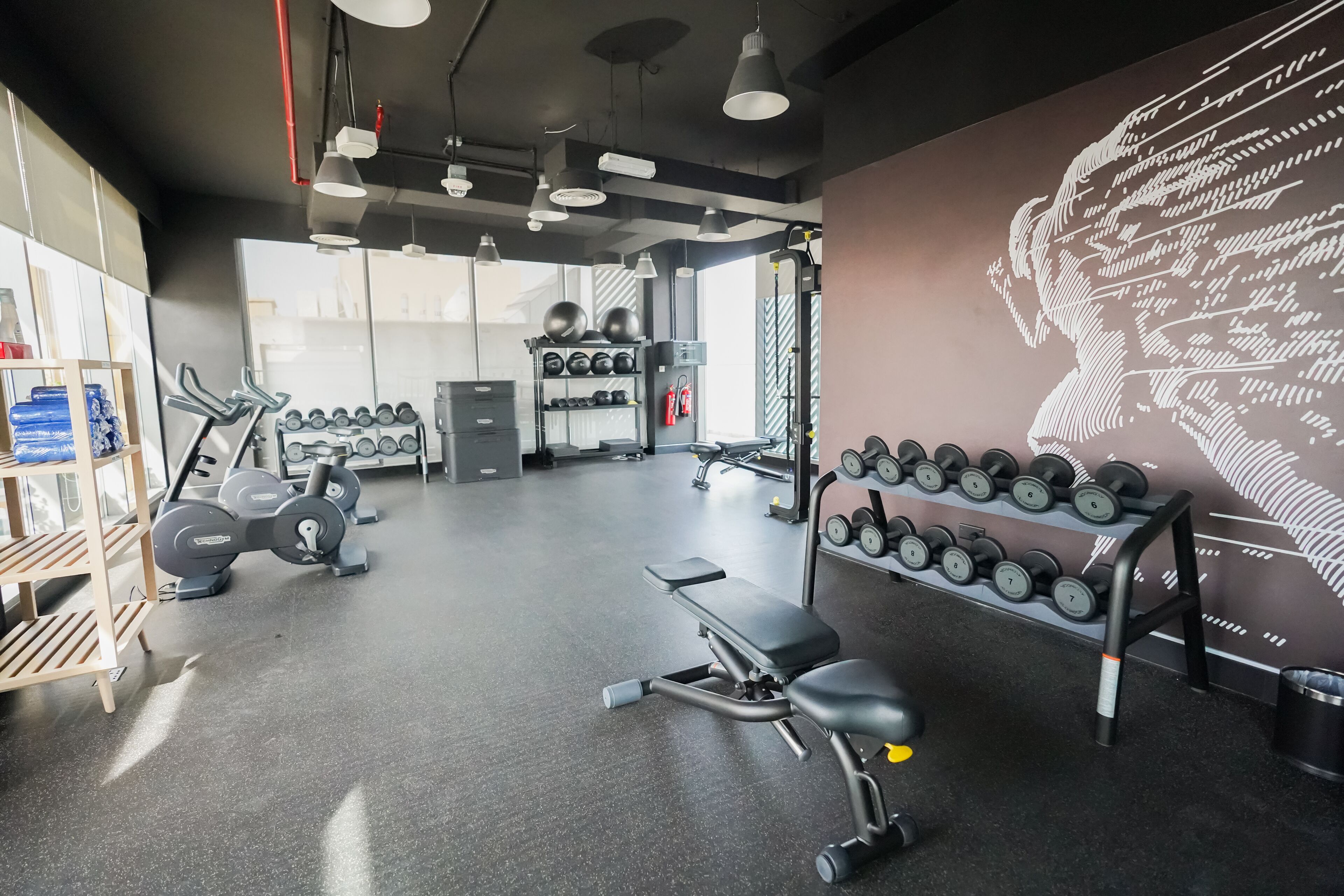 Une salle de sport équipée de matériel d’exercice, d’haltères et ornée d’une fresque murale.