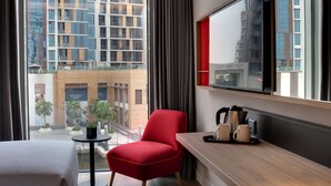 A hotel room with a large window, a red chair, a small table with a plant, and a tray with cups and a kettle. - IntercityHotel Dubai Jaddaf Waterfront (Dubai)