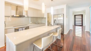 A modern kitchen with a central island, bar stools, stainless steel appliances, and pendant lighting. - Quay River Beach Hotel (Biggera Waters)