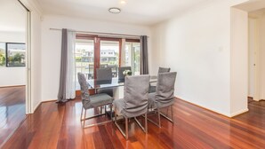 A dining area with a glass table and four chairs, a view of buildings outside, and wooden flooring. - Quay River Beach Hotel (Biggera Waters)