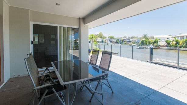 A balcony with a glass table and chairs, overlooking a marina with boats and houses. - Quay River Beach Hotel (Biggera Waters)