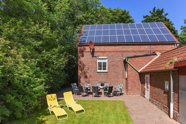 A brick building with a solar panel roof, a patio with chairs, and a lawn.