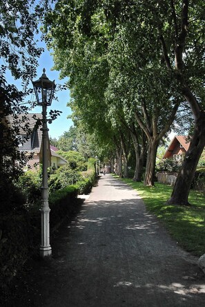 A tree-lined pathway with a lamp post and houses in the background. - Holiday house North Sea magic (Esens)