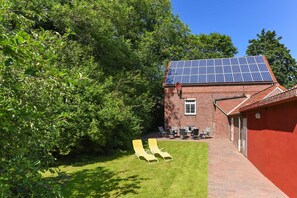 A brick building with a solar panel roof, a grassy lawn, and two yellow lounge chairs. - Holiday house North Sea magic (Esens)