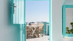 An open door leading to a terrace with a table and chairs, a view of the sky, and a window with a plant. - Cave Agapi house with private hot tub and view of the Oia caldera (Oia)