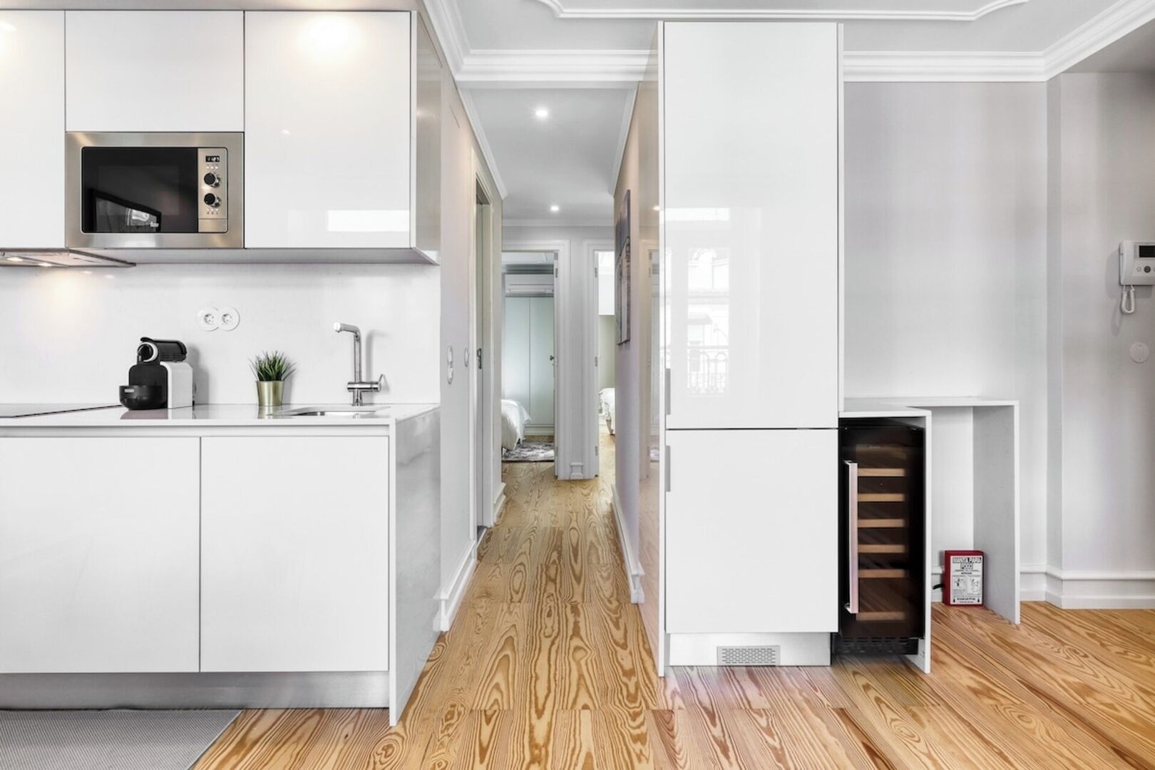 A modern kitchen with white cabinetry, a built-in microwave, and a wooden floor.
