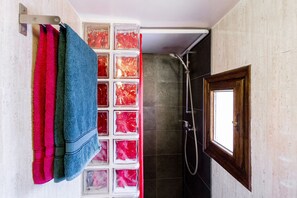 Casa de banho com chuveiro, janela e um porta-toalhas com vários toalhas.