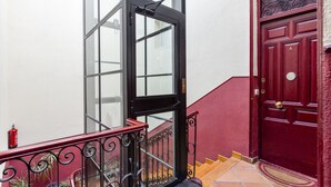 Une porte rouge avec un bouton de porte en laiton, une porte en verre avec un cadre noir et un garde-corps métallique rouge agrémenté d’éléments décoratifs.