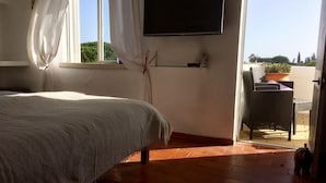 Una camera da letto con un letto, una TV montata a parete e vista sull'esterno attraverso una porta aperta.