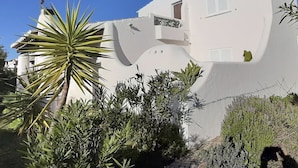Un edificio bianco con una facciata curva particolare, un piccolo balcone e vegetazione circostante.