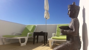 Una terrazza con due poltrone verdi imbottite, un tavolino e una statua.