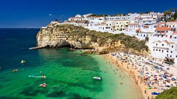 Una località costiera con spiaggia, acque cristalline e edifici bianchi.