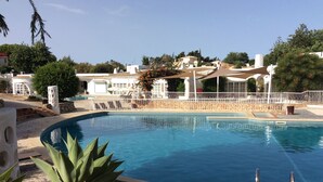 Una piscina con bordo in pietra, circondata da un recinto bianco e alcune piante sullo sfondo.