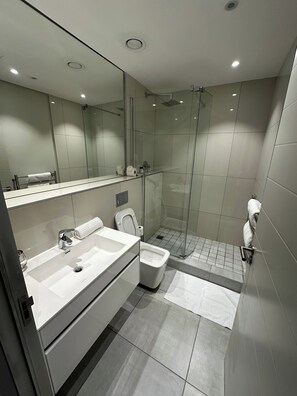 A modern bathroom with a glass-enclosed shower, a dual sink vanity, and a toilet. - Urban Elephant At The Docklands (Cape Town)