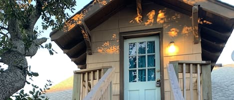 A wooden staircase leading to a cabin with a door and windows, surrounded by trees.