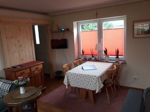 Un coin repas avec une table dressée pour quatre personnes, entourée de chaises en bois. Un téléviseur est fixé au mur, au-dessus de la table.