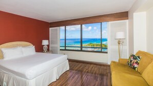 A hotel room with a bed, a sofa, and a large window offering a view of the ocean and a beach. - Discovery Bay Ocean View Studio, Near the Beach! (Honolulu)