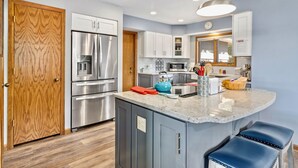A modern kitchen with stainless steel appliances, a wooden door, and a blue island with stools.