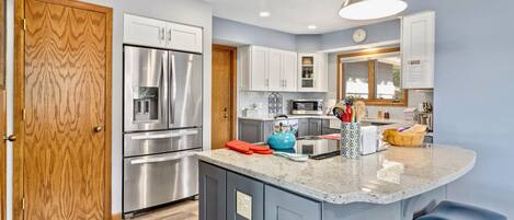 A modern kitchen with stainless steel appliances, a wooden door, and a blue island with stools.
