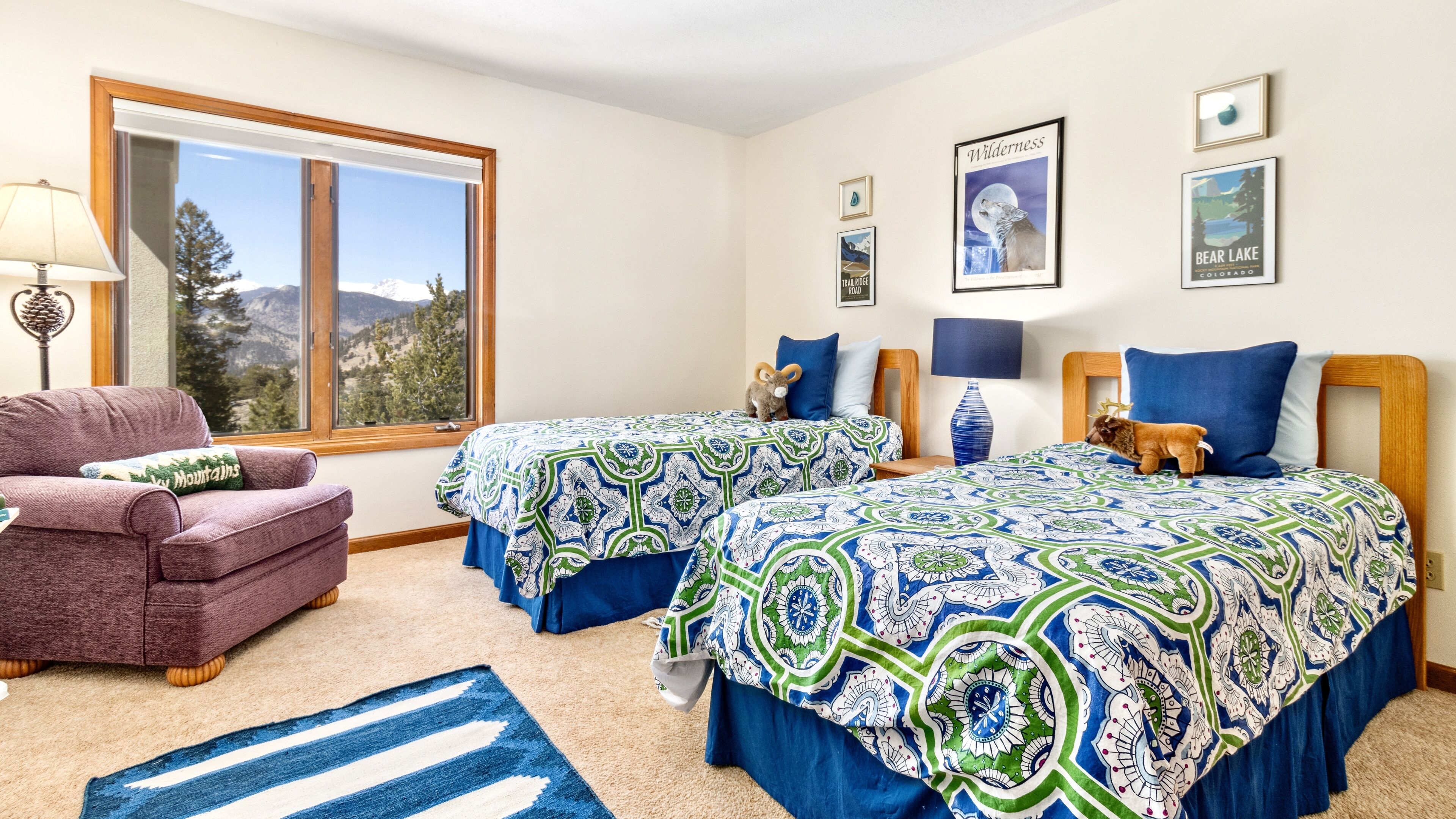 A bedroom with two beds, a window with a mountain view, a chair, and a lamp.